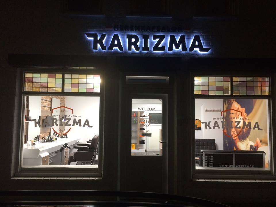 De winkelpui bij avond met de verlichte KARIZMA-letters boven de ramen